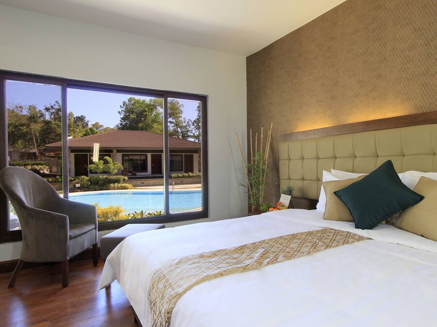 Habitación de hotel con una cama grande, una silla y vista a una piscina.