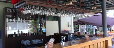 Zona de bar con mostrador de madera, lámparas colgantes y vistas al exterior.
