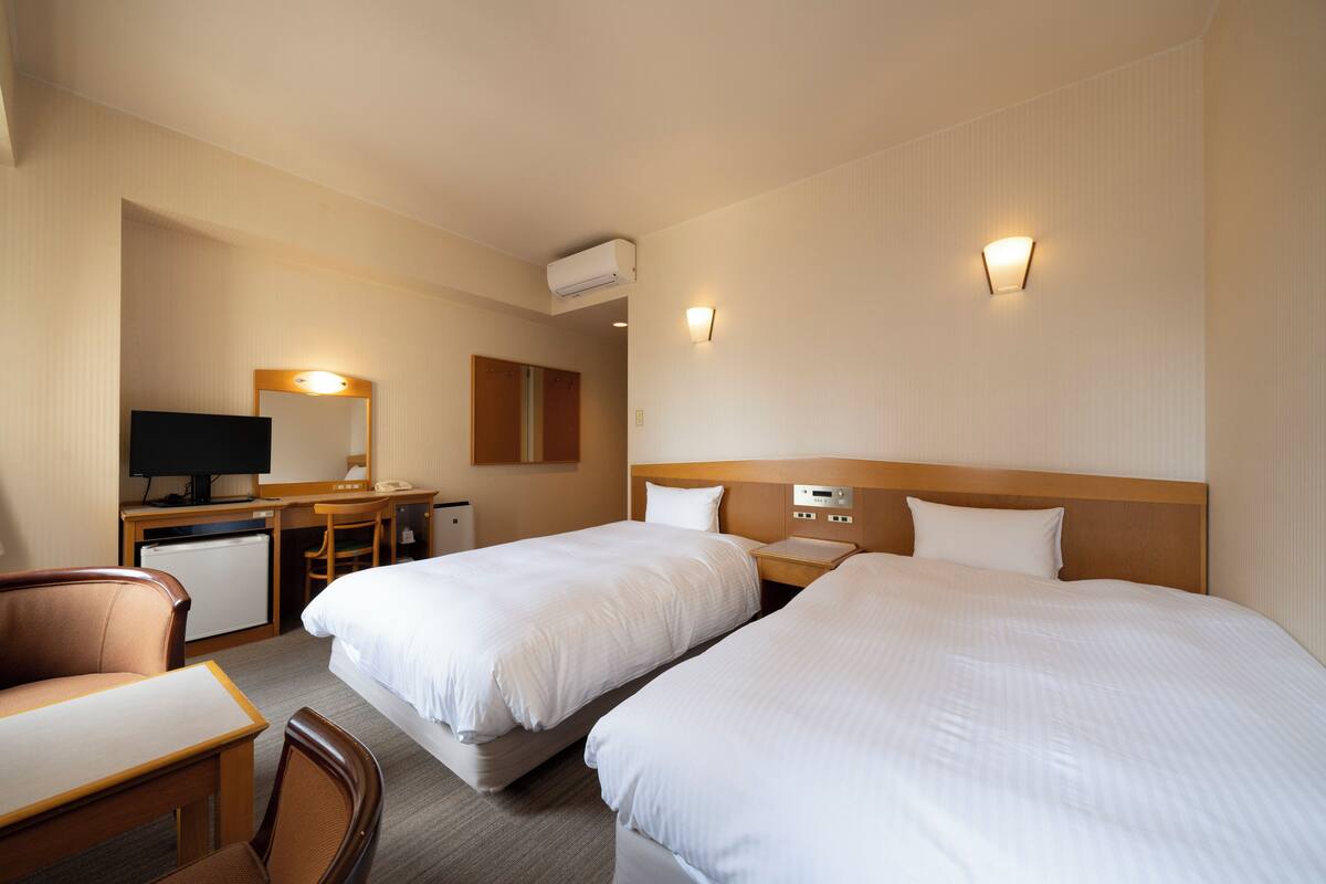 Une chambre d’hôtel avec deux lits, un bureau, une chaise, une télévision et un petit réfrigérateur.