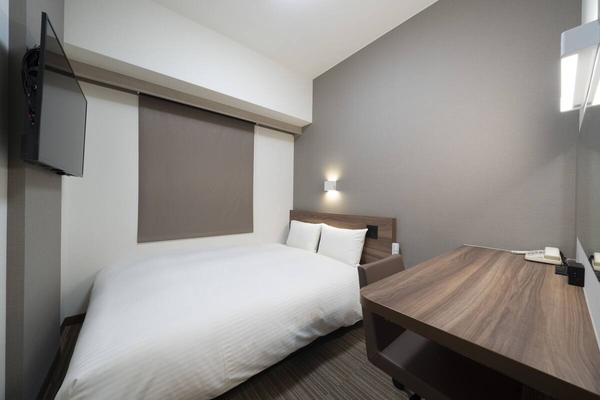 Une chambre d’hôtel équipée d’un lit, d’un bureau, d’un téléviseur fixé au mur et d’une lampe fixée au mur.