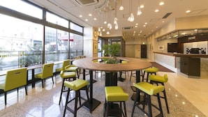 A modern dining area with a round table surrounded by yellow chairs, large windows, and a view of the city. - Nagoya B's Hotel (Nagoya)