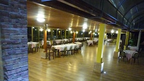 A spacious indoor dining area with multiple tables and chairs, wooden flooring, and large windows. - La Valle Verde (Zambrone)
