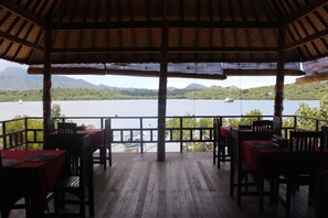 An outdoor dining area with tables and chairs, overlooking a body of water and mountains.