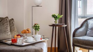 A neatly arranged breakfast tray with croissants, fruits, and beverages on a bed in a modern room with a sofa and a small table with a vase. - Relais Rione Ponte (Rome)
