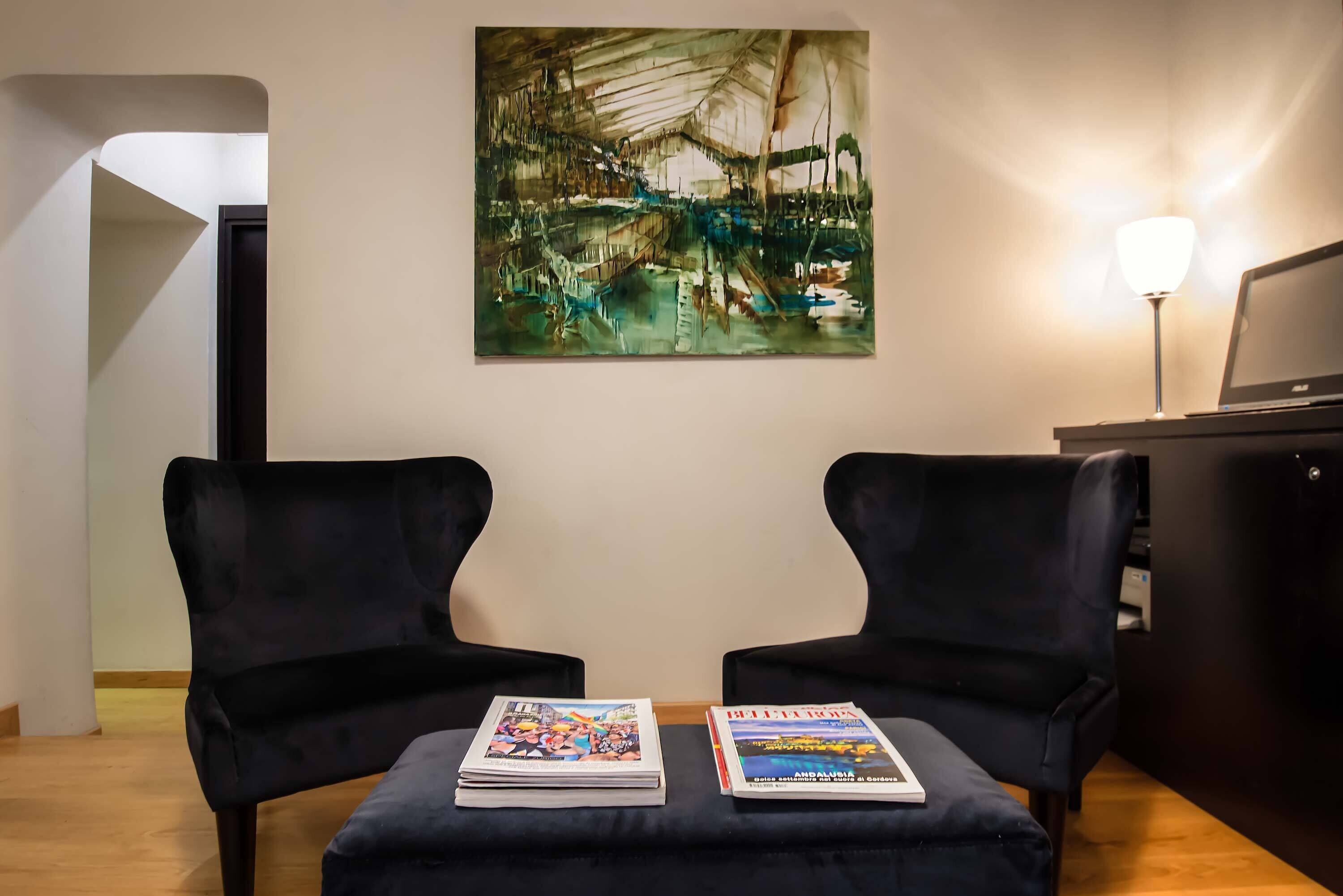 Una habitación con dos sillones negros, un cuadro en la pared y una lámpara sobre una mesa.