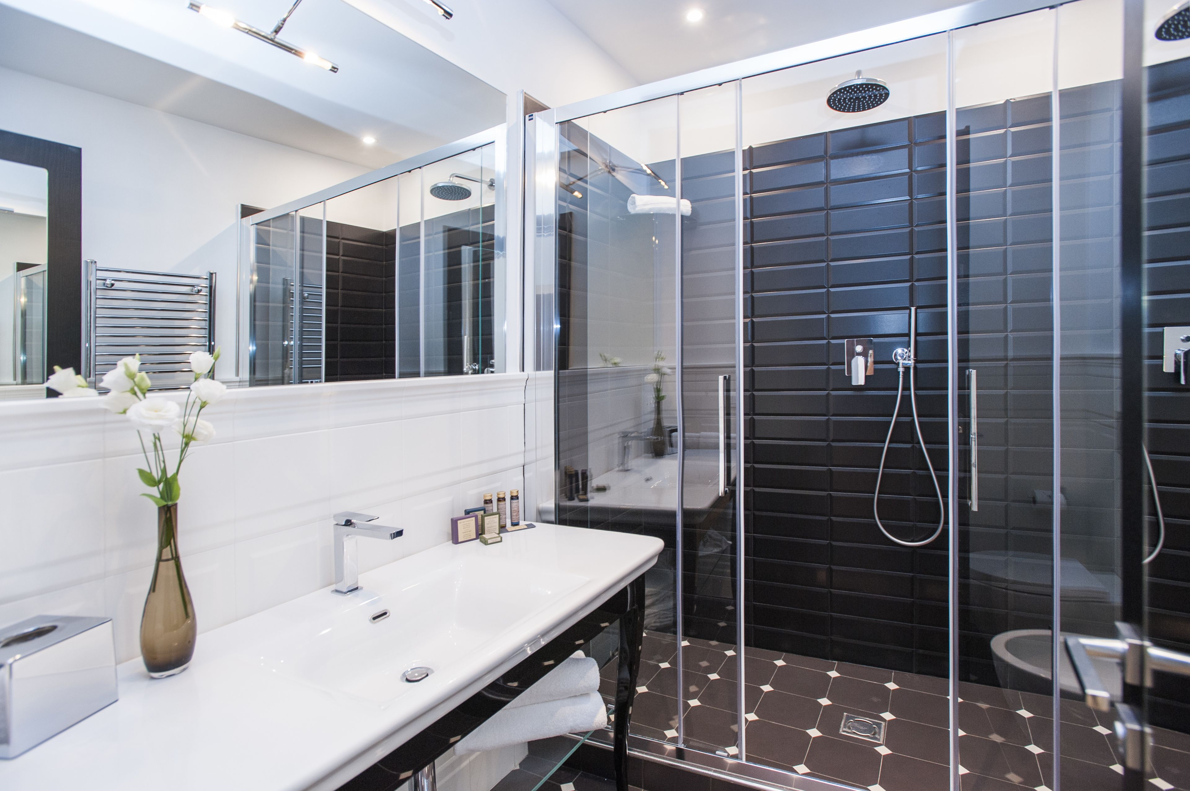 A modern bathroom with a glass-enclosed shower, a white vanity, and a vase with flowers.