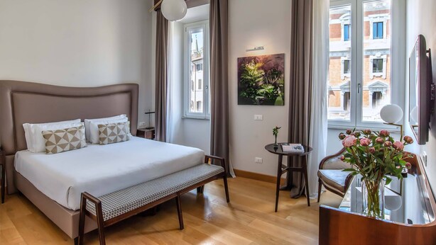 A hotel room with a large bed, a small table, a chair, a mirror, and a window with a view of buildings. - Relais Rione Ponte (Rome)