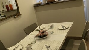 A dining area with a table set for four, a mirror, a shelf with kitchen items, and a window with blinds. - Art Atelier Accomodation (Rome)