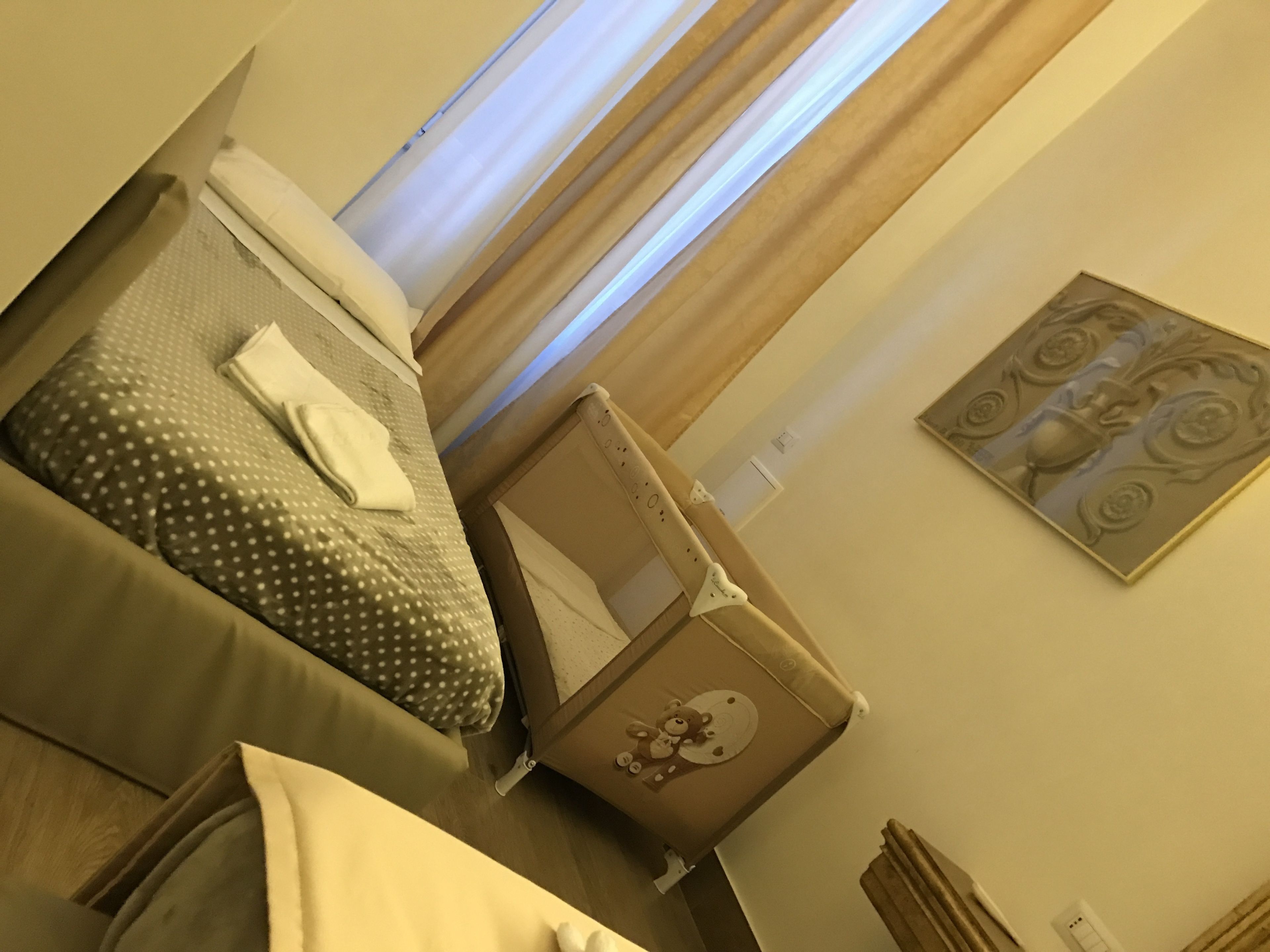 A hotel room with a bed, a bedside table, a wall-mounted artwork, and a window with curtains.