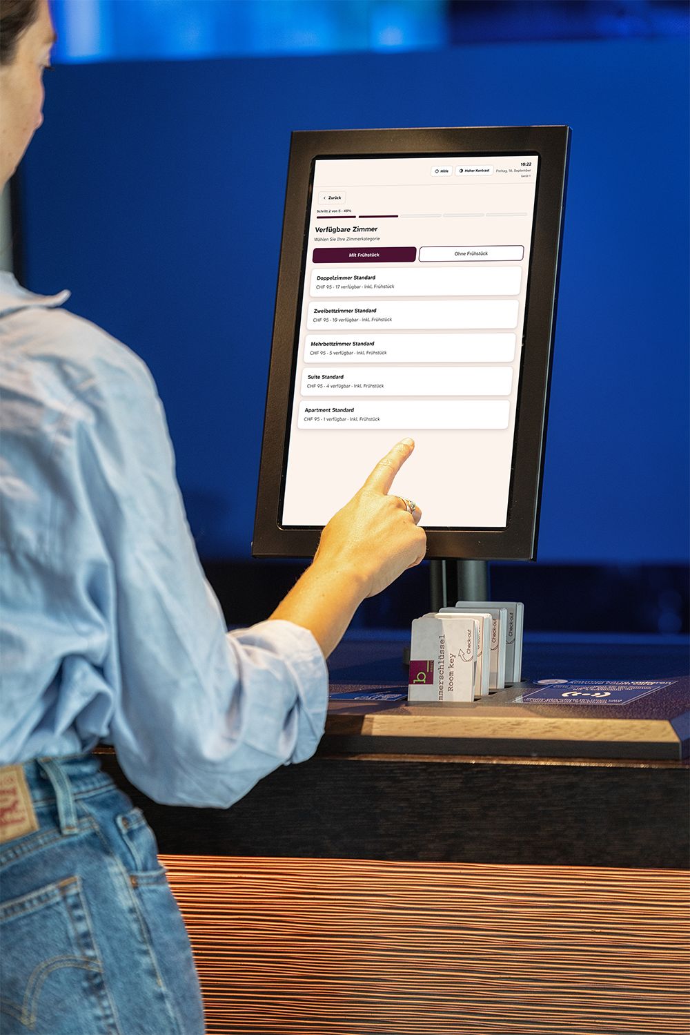 A person interacting with a digital display at a hotel reception desk.