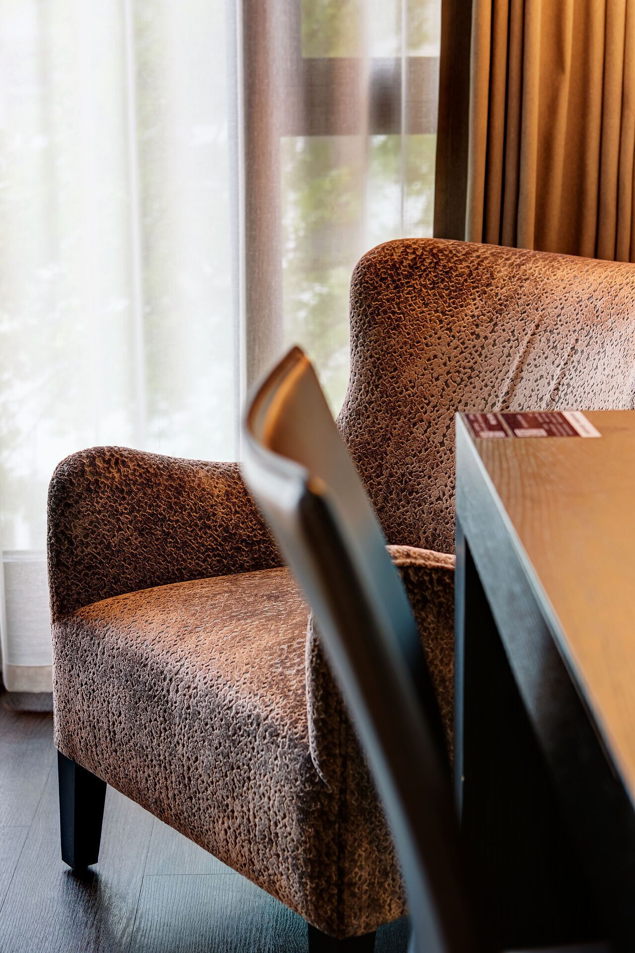 Una silla con tela texturizada, una mesa de madera y una ventana con cortinas.