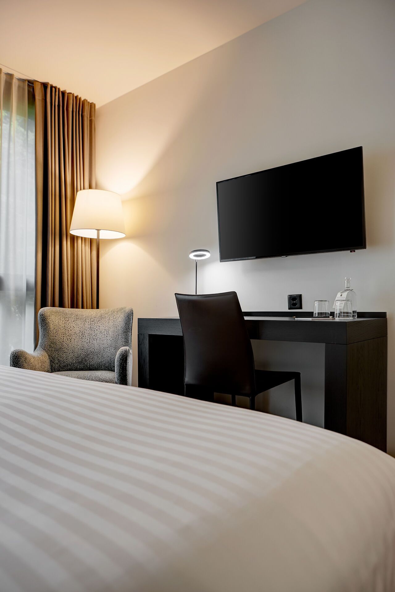Una habitación de hotel con cama, escritorio, silla, televisor y lámpara.