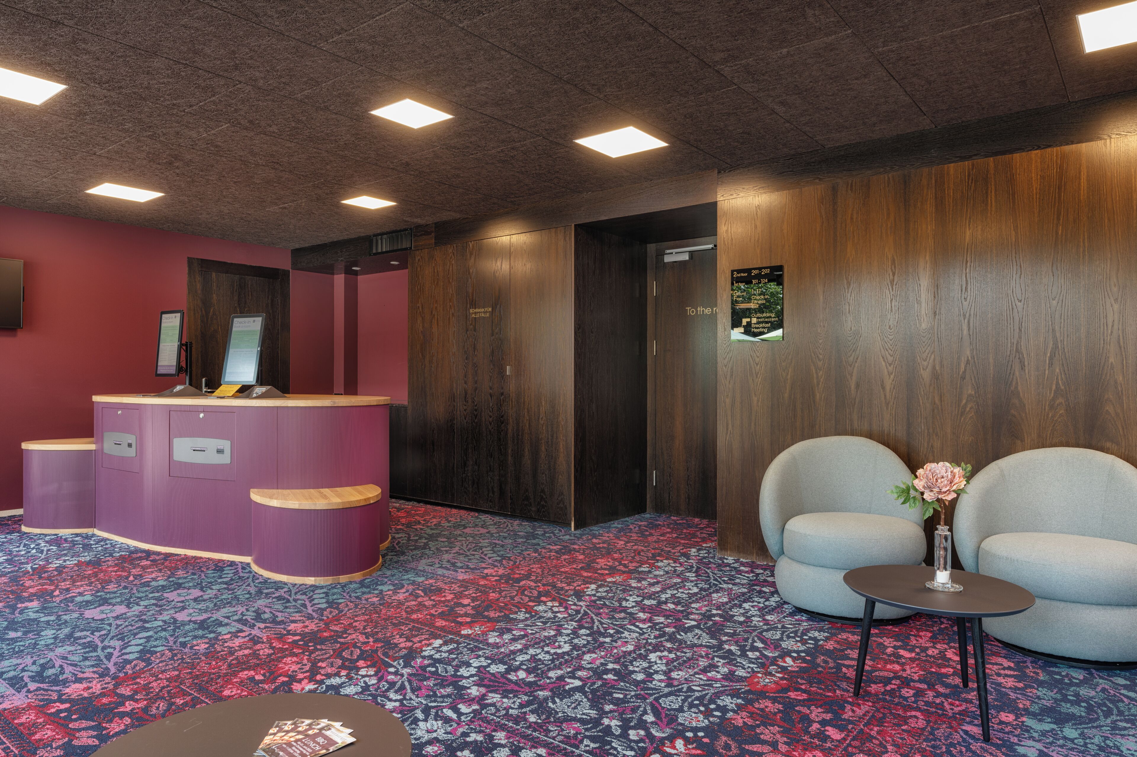 Un área de recepción con un mostrador curvo, dos sillones, una mesita con un florero y una alfombra estampada.