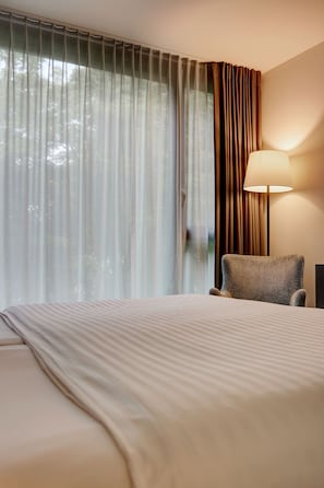 Une chambre dâhĂŽtel avec un lit, une chaise, une lampe et des rideaux en voile.