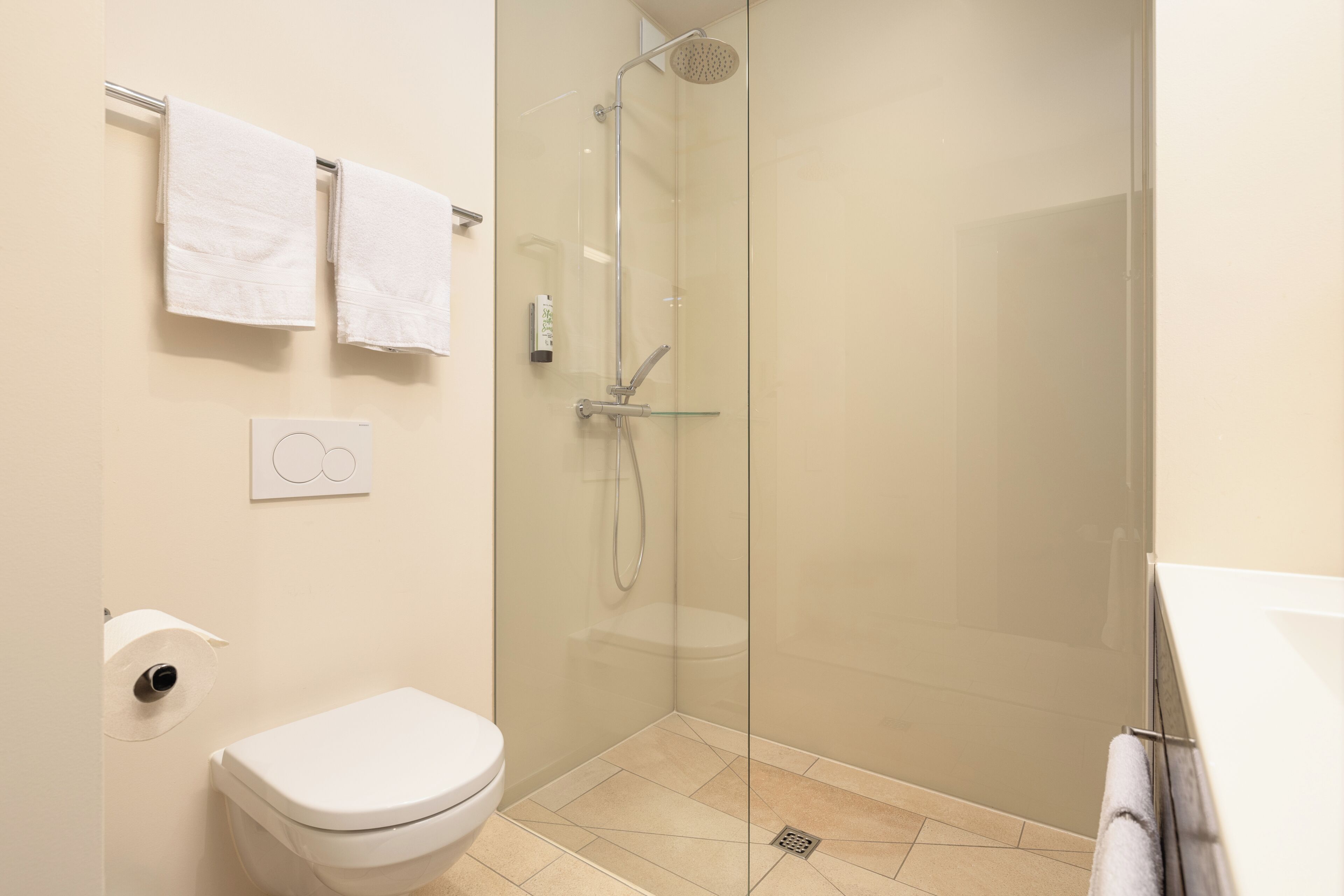A bathroom with a glass-enclosed shower, a toilet, and two towels on a rack.
