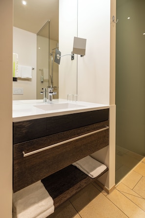 Une salle de bain avec un lavabo blanc, un meuble-lavabo en bois foncé, un porte-serviettes et une cabine de douche en verre.