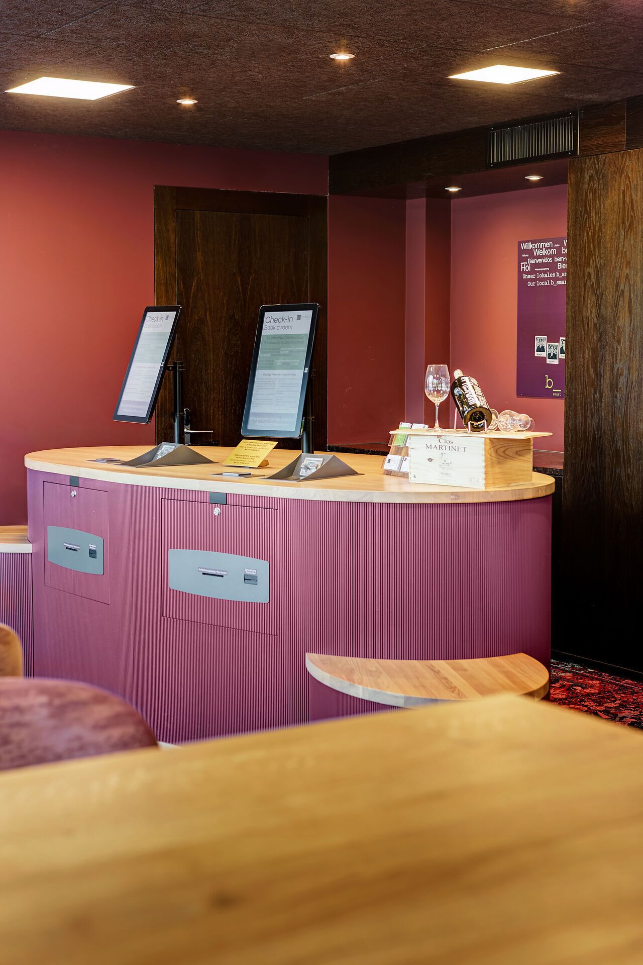 A reception desk with a check-in kiosk, a wine bottle, and a menu stand.