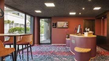Zona de recepción de un hotel, con mostrador de recepción, asientos y vistas al exterior.
