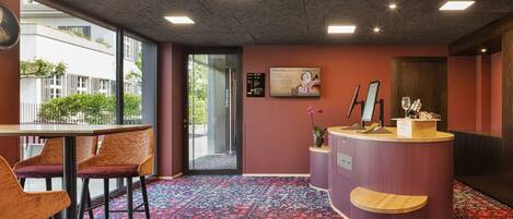 A hotel reception area with a check-in counter, seating area, and a view of the outside.