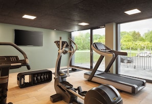 Une salle de sport Ă©quipĂ©e de machines de cardio, dâun banc de musculation et dâune grande fenĂȘtre donnant sur lâextĂ©rieur.