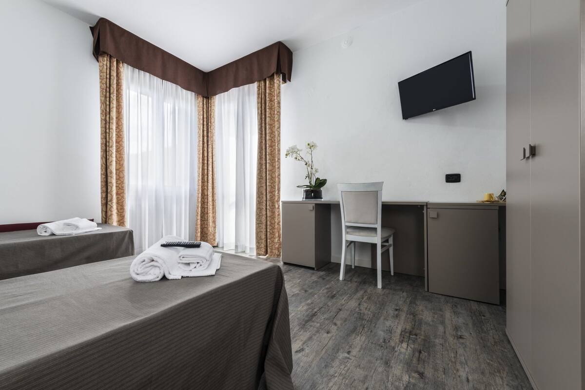A hotel room with two beds, a desk, a chair, a TV, and a potted plant.