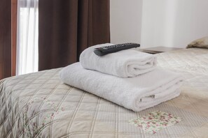 A neatly made bed with a quilted cover, a folded white towel, and a remote control on top. - Affittacamere Elena (Lazise)