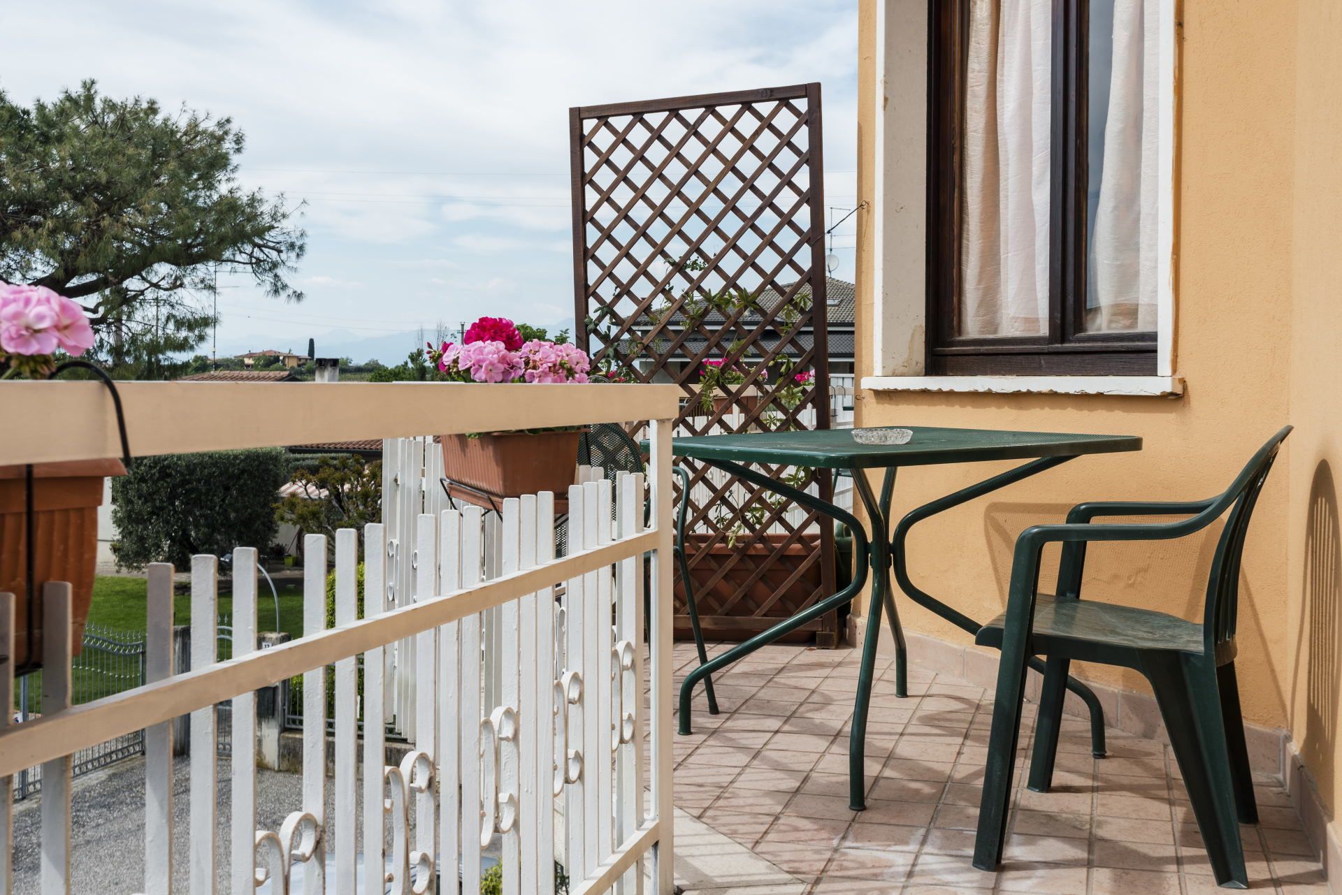 A balcony with a table and chairs, a white fence, and potted plants.