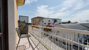 Un balcone con ringhiera bianca, una sedia verde e una pianta in vaso con fiori rosa.