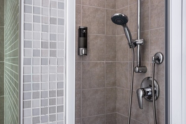 A modern shower with a handheld showerhead, a wall-mounted control panel, and a handheld shower attachment.