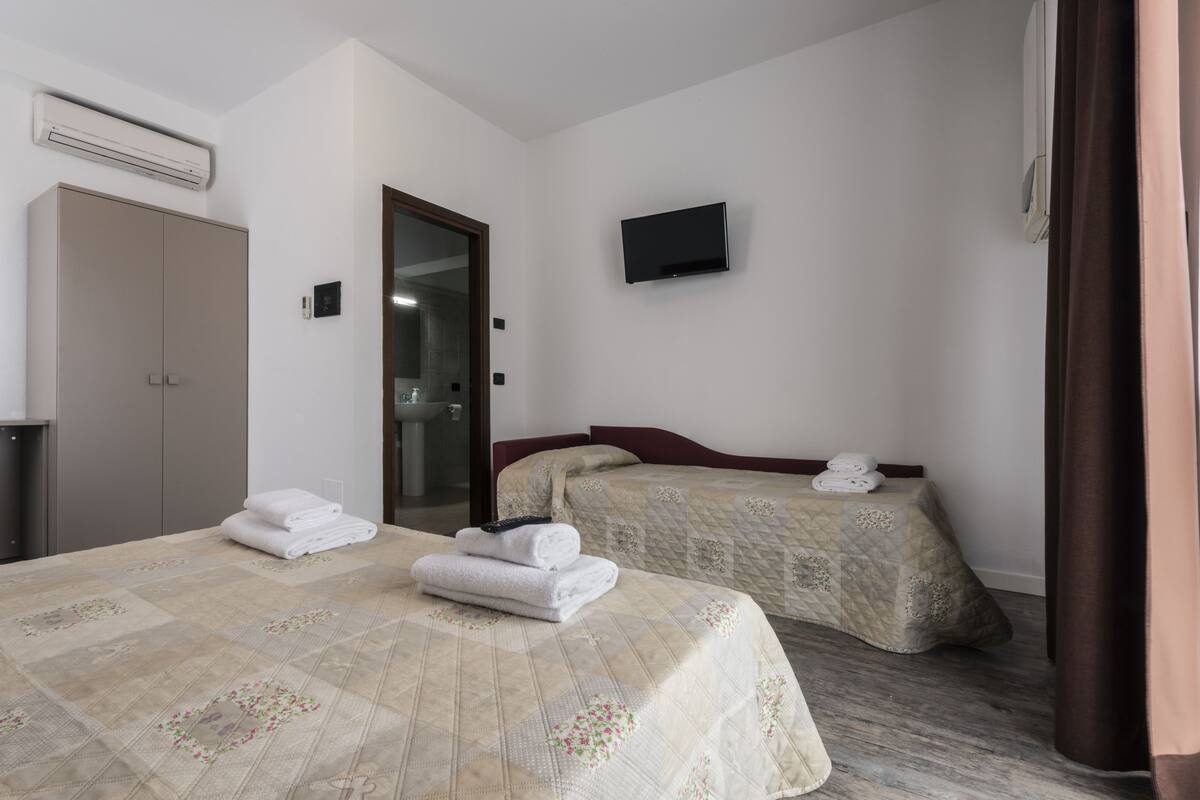 A hotel room with two beds, a TV, an air conditioning unit, and a door leading to a bathroom.