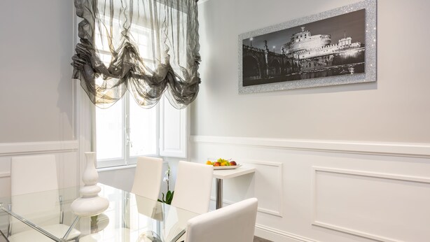A dining area with a glass table, white chairs, a white vase, and a framed black and white photo on the wall. - Residenza Vatican Suite (Rome)