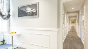 A hallway with a white wall, a framed black and white photo, a small white table with fruit, and a plant. - Residenza Vatican Suite (Rome)
