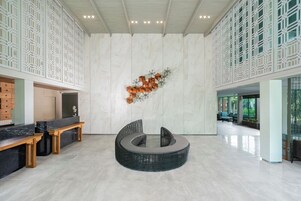 Un vestíbulo amplio con una zona de estar central, una recepción y una pared decorativa con patrones geométricos.