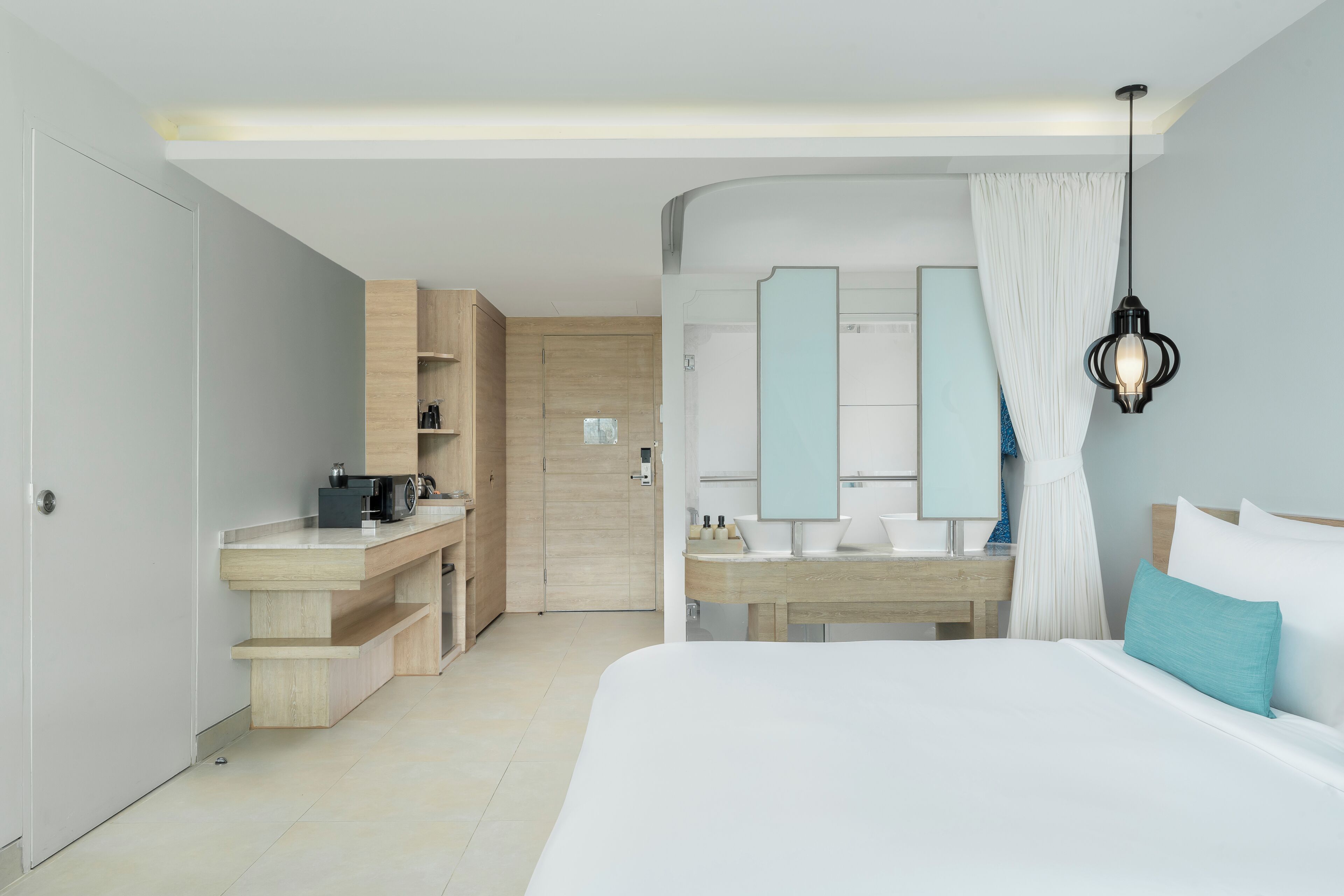 A modern hotel room with a bed, a bathroom with a mirror, a kitchenette, and a wooden cabinet.