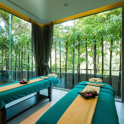 A room with two massage tables, each with a green towel and a wooden bench.