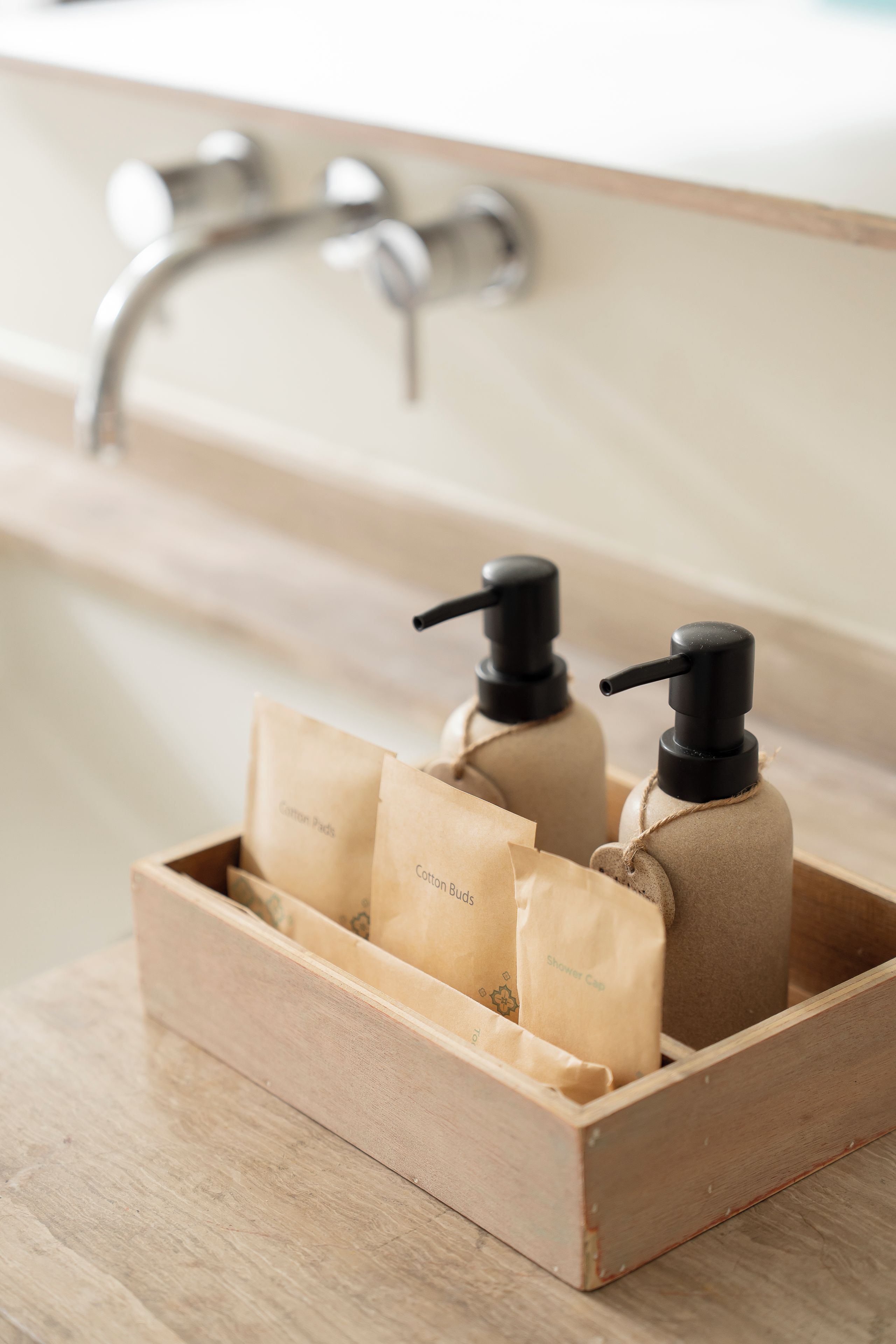 A wooden box with items labeled 'Cotton Pads' and 'Shower Cap' in a bathroom setting.