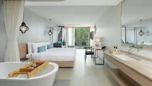 Een moderne hotelkamer met een groot bed, een aparte badkamer, een zithoek en uitzicht op groen buiten.