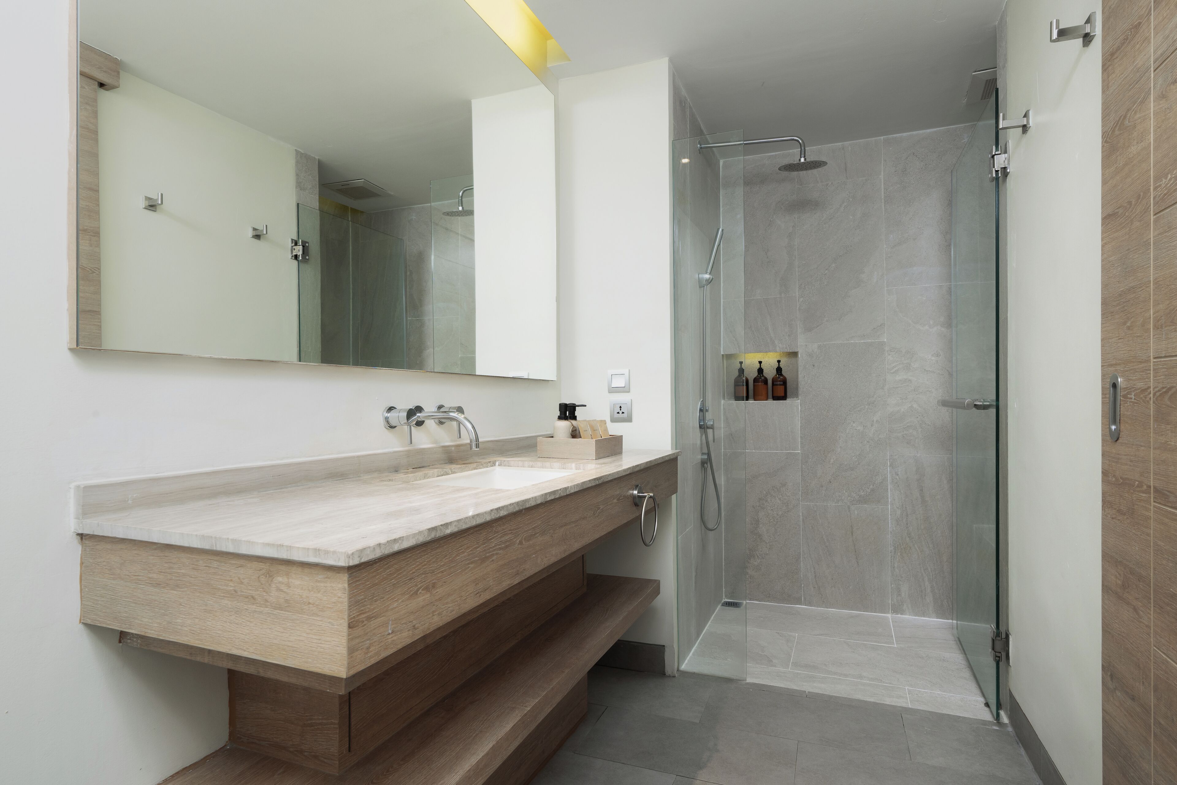 A modern bathroom with a wooden vanity, a large mirror, and a glass-enclosed shower.