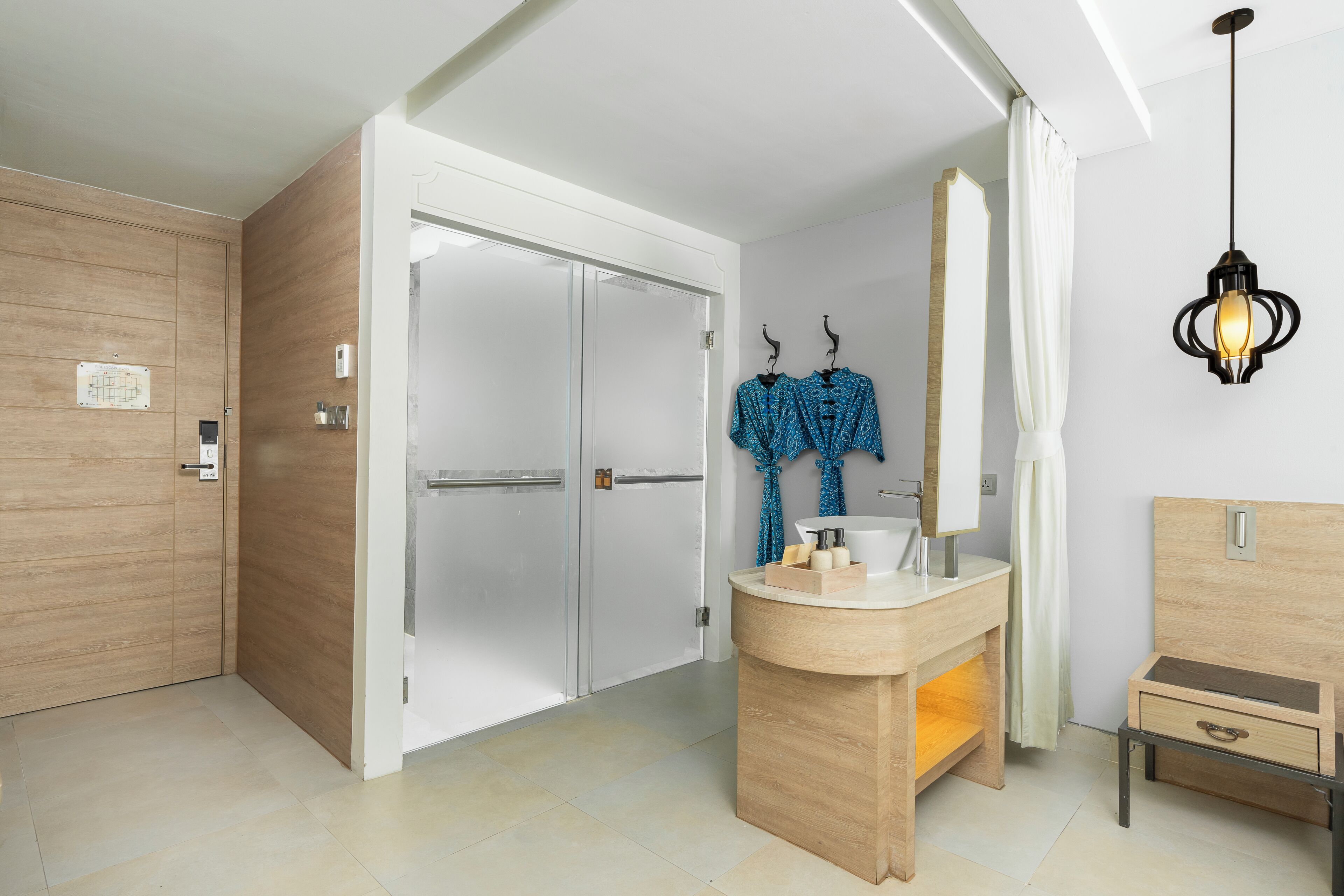 A modern bathroom with a wooden vanity, a glass shower enclosure, and a hanging light fixture.
