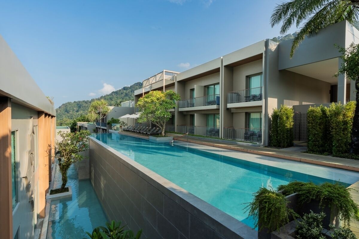 Un hotel moderno con piscina, varios balcones y abundante vegetación.