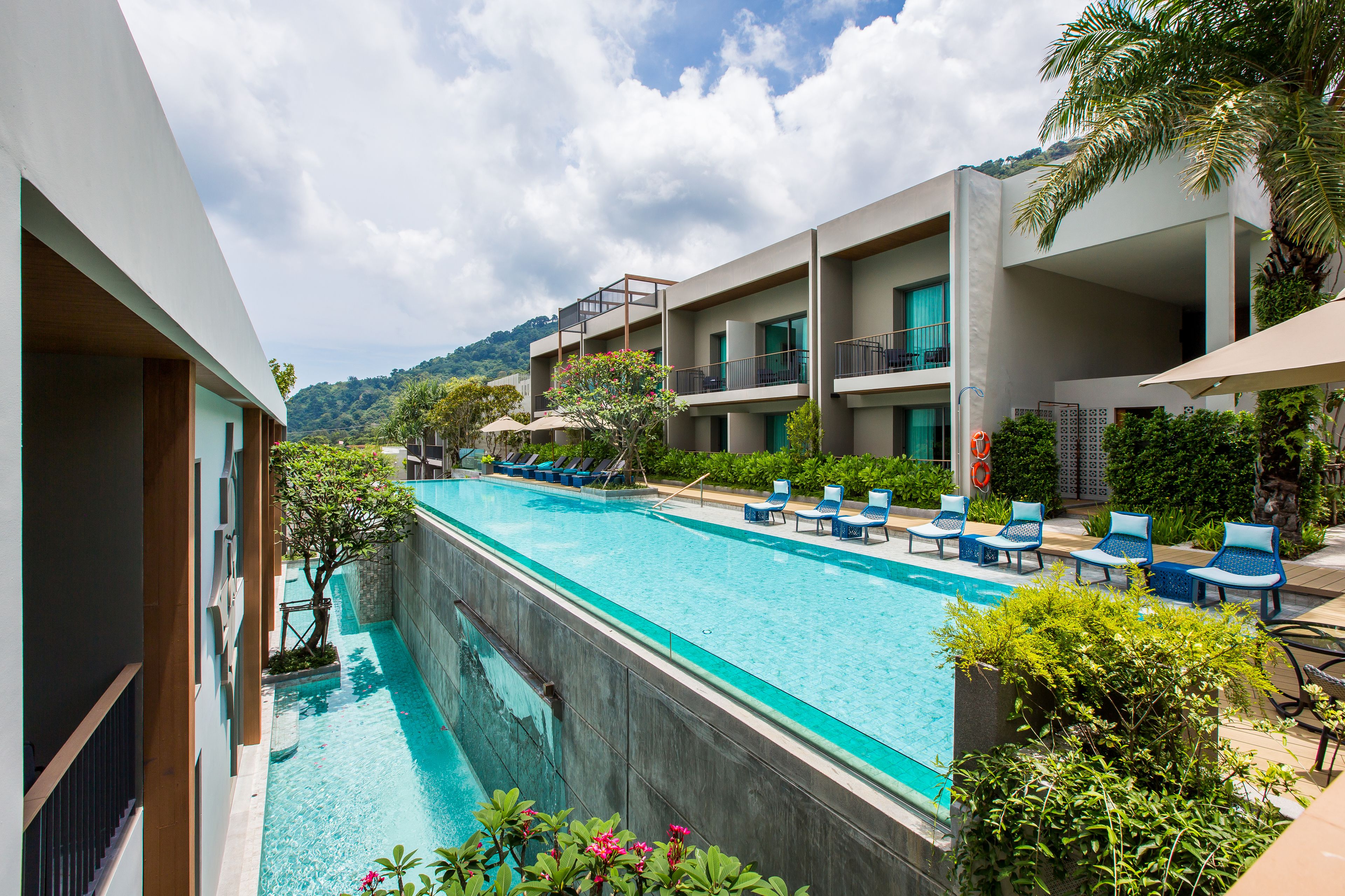 Un hotel moderno con piscina, varios balcones y abundante vegetación.