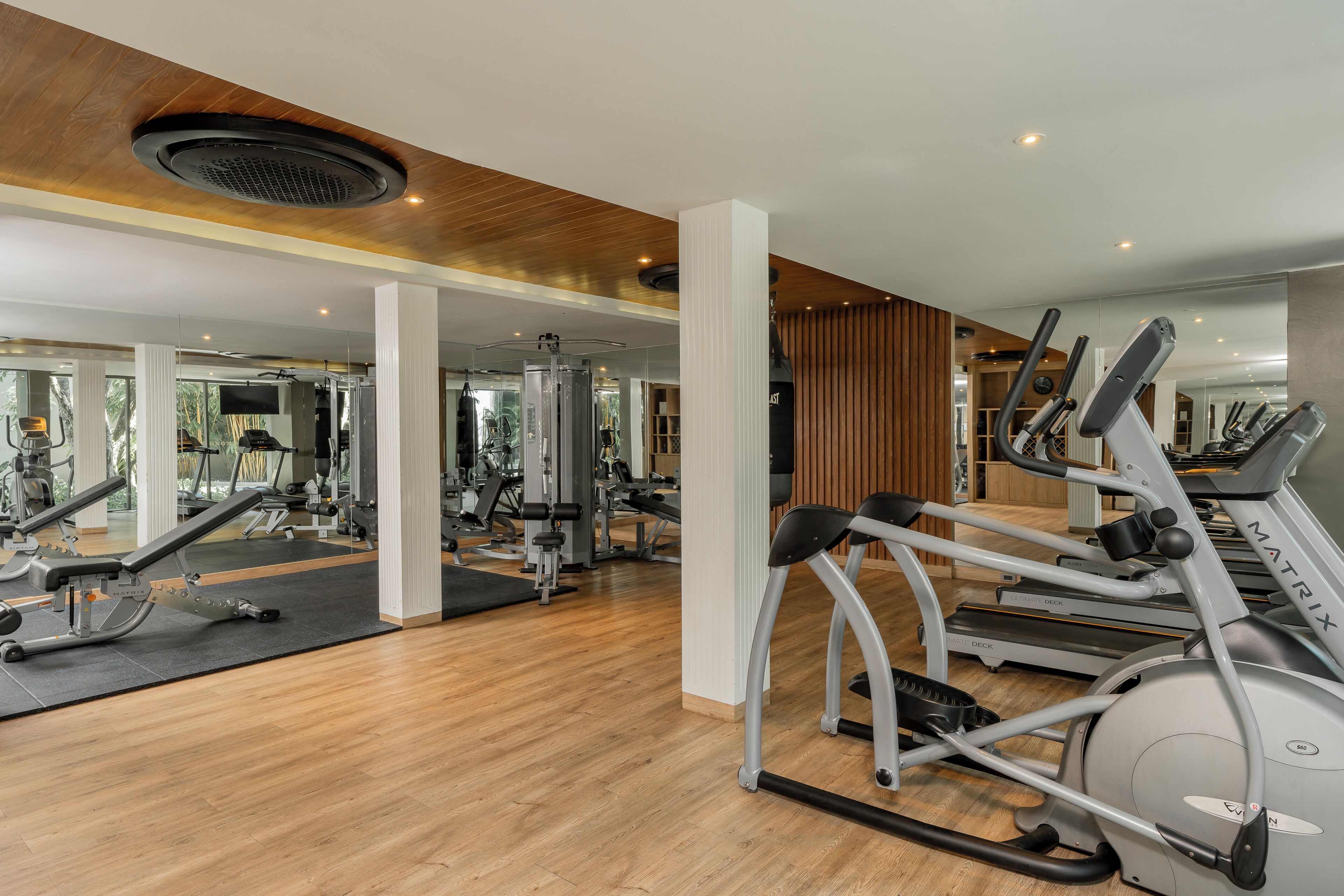 Academia com equipamentos de exercício, piso de madeira e parede com espelhos.