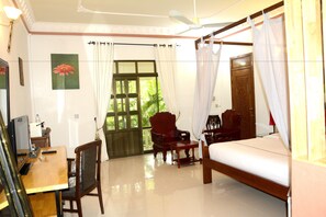 A hotel room with a bed, a desk, two chairs, a television, and a window with curtains. - Tropical Hill Kep (Kep)