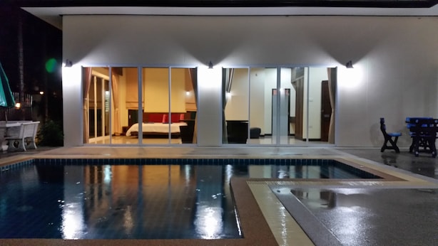 A hotel room with a large sliding glass door leading to a bedroom, a swimming pool, and a patio area with outdoor furniture.
