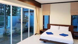 A bedroom with a large bed, sliding glass doors to a balcony, and a view of the outdoors.