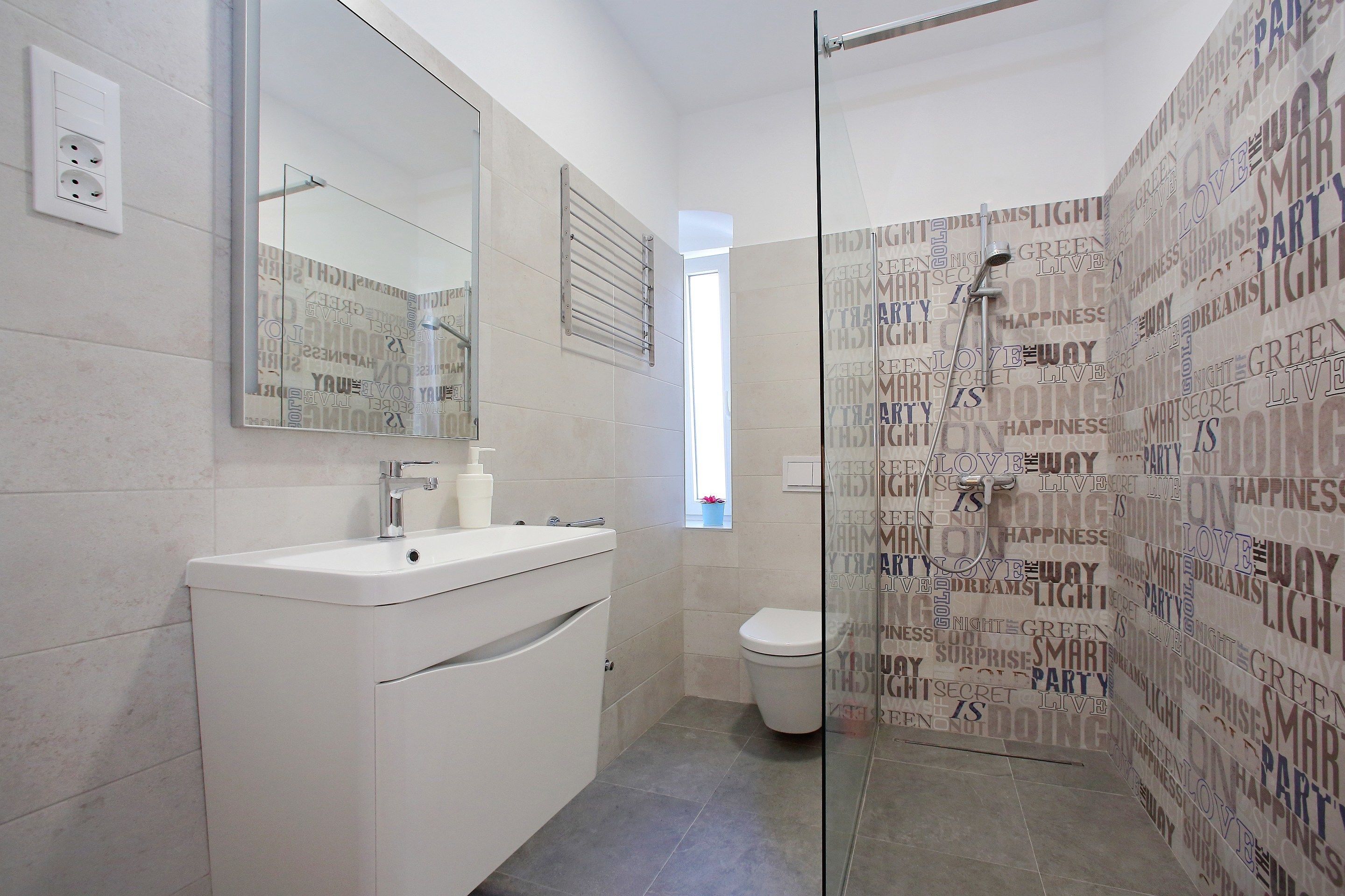 Un baño moderno con lavamanos blanco, espejo y cabina de ducha de vidrio.
