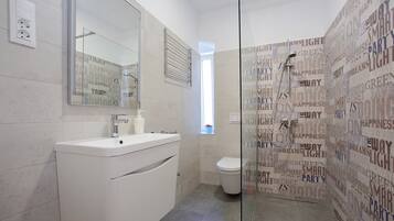 Uma casa de banho moderna com lavatório branco, espelho e cabine de duche em vidro.