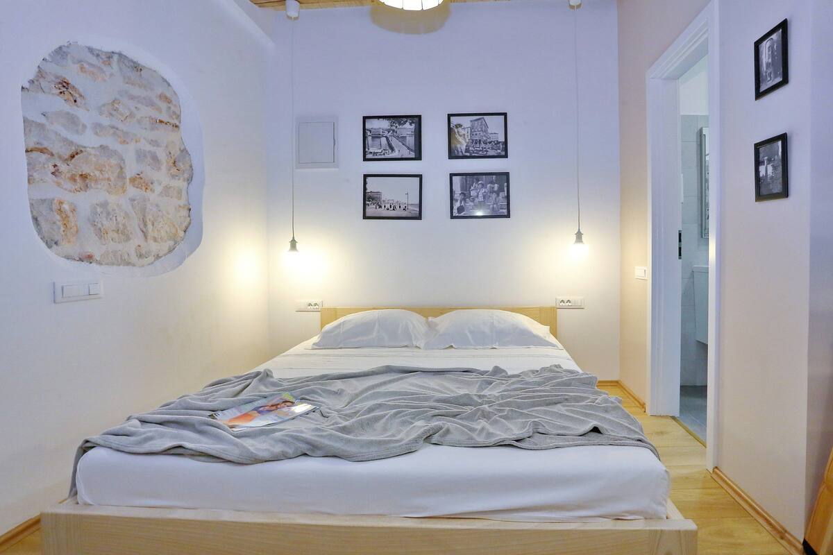 Ein Schlafzimmer mit einem Bett, einer Steinwand und vier gerahmten Bildern an der Wand.