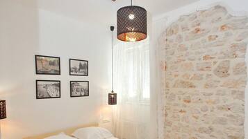 Un dormitorio con piso de madera, una cama con sábanas blancas, una lámpara colgante y una pared de piedra.