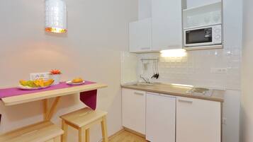 A compact kitchen with white cabinets, a microwave, a sink, and a wooden table with a pink placemat.